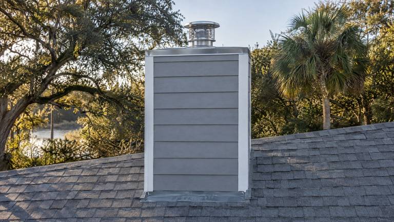 A chimney chase with gray lap siding, white corner boards and a stainless chase cover with a round cap.