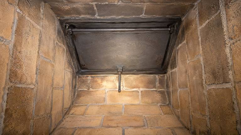 Looking up at a cast-iron damper plate closed in its frame above a clean firebrick firebox.